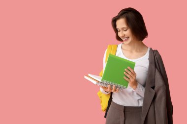 Pembe arka planda not defterleri ve sırt çantası olan güzel bir kız öğrenci.