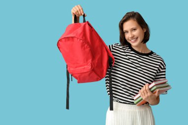 Sırt çantası ve mavi arka planda defterleri olan mutlu kız öğrenci.