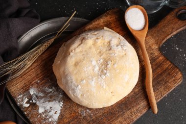 Tahta tahtada taze hamur, buğday ve kaşık şeker var.