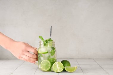 Beyaz arka planda bir kavanoz taze Mojito kokteyli ile kadın eli.