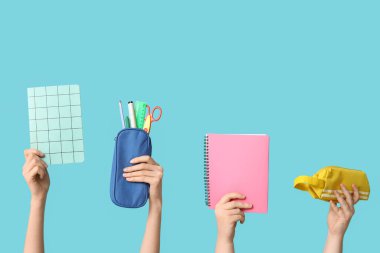 Mavi arka planda kırtasiyeli defter ve kalem kılıfları tutan kadın eller.