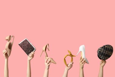 Torba, kep, saç bandı ve pembe arka planda farklı topuklu ayakkabılar olan kadın elleri.