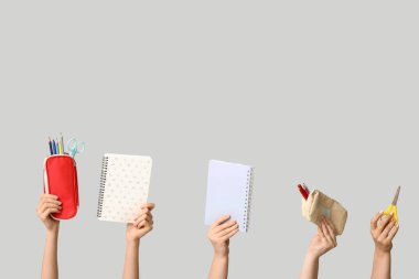 Gri arkaplanda kırtasiyeli defter ve kalem kılıfları tutan kadın eller