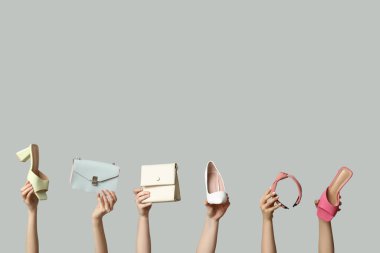 Saç bandı, çantalar ve gri arka planda farklı topuklu ayakkabılar olan kadın elleri.