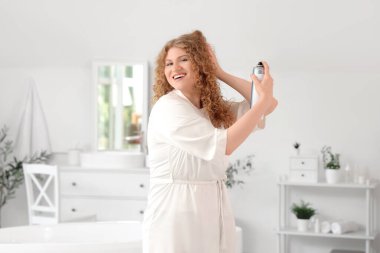 Evdeki banyoya saç spreyi sıkan genç ve güzel bir kadın.