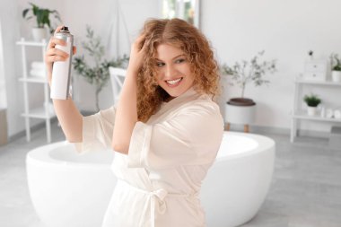 Evdeki banyoya saç spreyi sıkan genç ve güzel bir kadın.