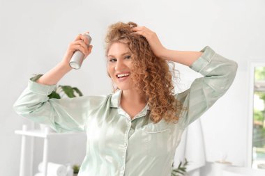 Evdeki banyoya saç spreyi sıkan genç ve güzel bir kadın.