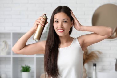 Güzel, genç, mutlu bir kadın evde saç spreyi sıkıyor.
