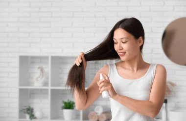 Güzel, genç, mutlu bir kadın evde saç spreyi sıkıyor.