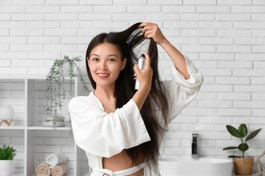 Güzel, genç, mutlu bir kadın evde saç spreyi sıkıyor.