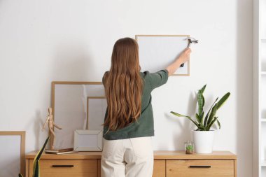 Oturma odasındaki duvara çerçeveyi asan genç bir kadın.