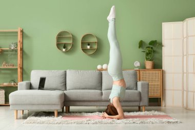 Güzel genç bir kadın oturma odasında yoga yapıyor.