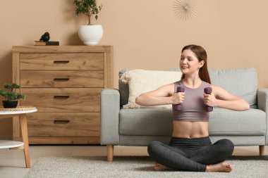 Oturma odasında dambıllarla antrenman yapan güzel bir genç kadın.