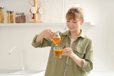 Genç bir kadın mutfaktaki çaya bal ekliyor.