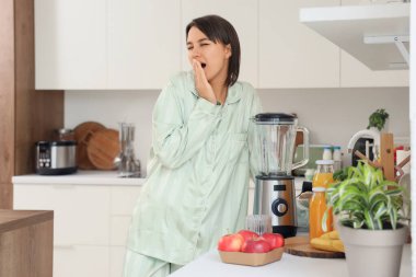 Mutfakta blenderi olan uykulu genç bir kadın.