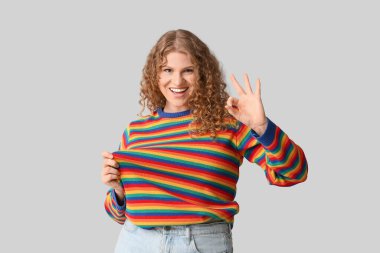 Gökkuşağı süveterli güzel bir kadın gri arka planda iyi niyet gösterisi yapıyor.