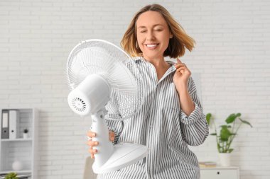 Ofisinde elektrikli yelpazesi olan güzel, olgun, mutlu bir iş kadını.