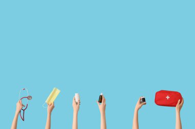 Tıbbi maskeli eller, steteskop, ilk yardım çantası, burun damlası ve mavi arka planda haplar.