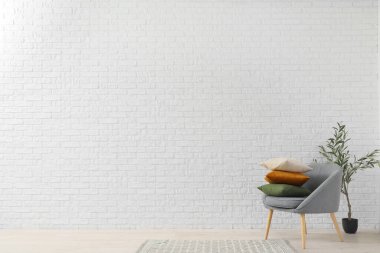 Yastıklı koltuk ve beyaz tuğla duvarın yanında dekoratif zeytin ağacı.