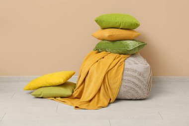 Yatak odasındaki bej duvarın yanında ekoseli yastık yığını.