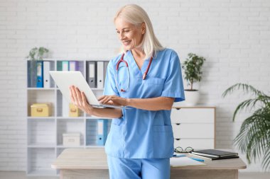 Klinikte dizüstü bilgisayarla çalışan olgun bir kadın doktor.