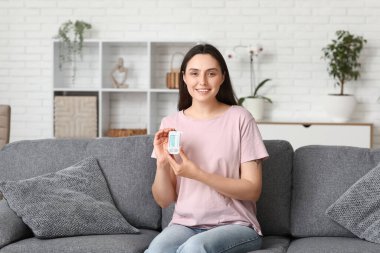 Glukometresi olan şeker hastası genç bir kadın evdeki kanepede oturuyor.