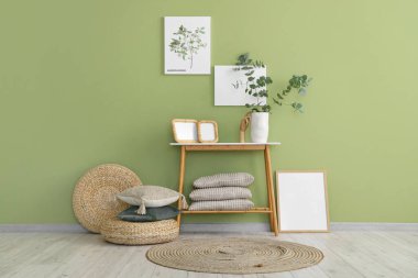 Okaliptüs dalları ve yeşil duvarın yanındaki bankta duran fotoğraf çerçeveli vazo.