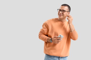 Gri arka planda cep telefonu olan kulaklıklı yakışıklı genç adam.
