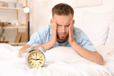 Stresli genç adam evde saatle yatakta yatıyor. Uykusuzluk kavramı