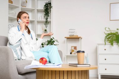 Evde elma ve kahveyle cep telefonuyla konuşan genç bir tıp öğrencisi.