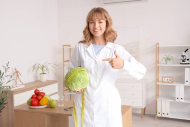 Kadın beslenme uzmanı ofiste mezurayla lahanayı işaret ediyor.