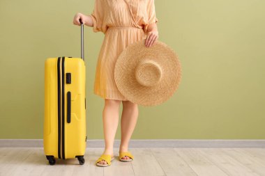 Yeşil arka planda hasır şapkalı ve bavullu genç bir kadın.