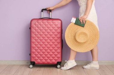 Bavulu, şapkası, pasaportu ve leylak arka planda bileti olan genç bir kadın.