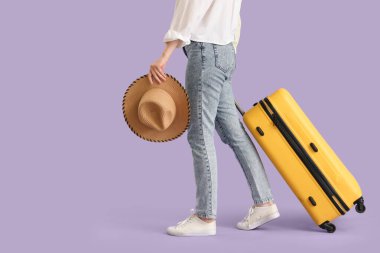 Leylak arka planda bavulu ve şapkası olan genç bir kadın.