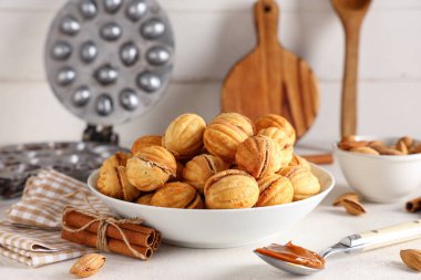 Lezzetli ceviz şekilli kurabiyeler, tarçın, badem ve ahşap masa üzerinde pişirme biçimi olan bir kase.