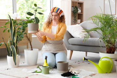 Evde yeşil bitkiyle ilgilenen genç bir kadın.