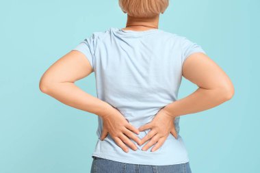 Mavi arka planda sırt ağrısı çeken olgun bir kadın. Arka plan