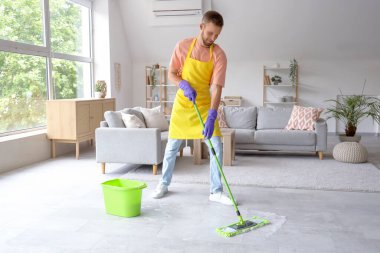 Erkek hademe, ışık odasında paspasla yerleri temizliyor.