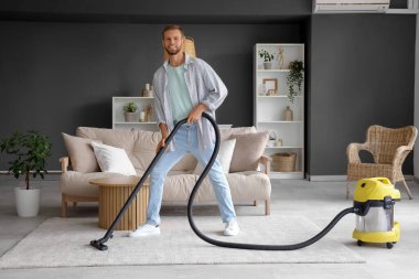 Erkek temizlikçi odada elektrikli süpürgeyle yerleri temizliyor.