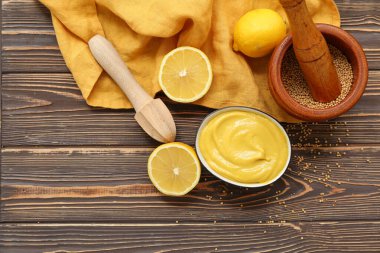 Kahverengi ahşap arka planda bir kase kremalı hardal ve limon.