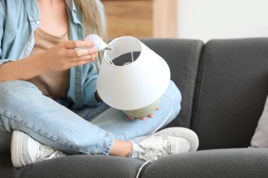 Genç bir kadın evdeki kanepede ampulü lambaya sıkıştırıyor.