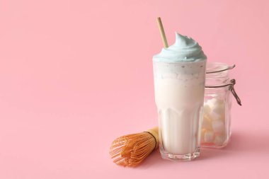 Bir bardak mavi dalgona matcha latte, rafine şekerli kavanoz ve pembe arka planda chasen.