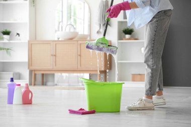 Kovalı ve deterjanlı genç bir kadın evde yerleri paspaslıyor.