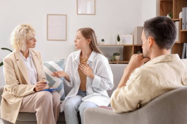 Kadın psikolog ofiste genç bir çiftle konuşuyor.