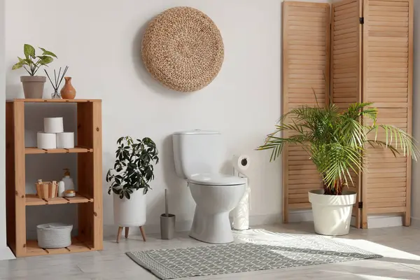 Tuvaletin içinde tuvalet, katlanan ekran, bitkiler ve raflar beyaz duvarın yanında.