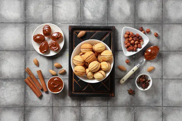 Lezzetli ceviz şekilli kurabiyeler, kaynamış süt ve gri kiremitli masada bulunan malzemeler.