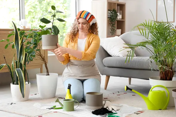 Evde yeşil bitkiyle ilgilenen genç bir kadın.