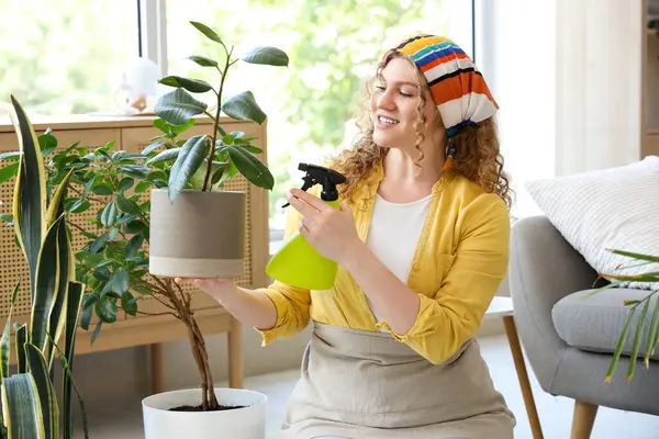 Evde yeşil bitkiyle ilgilenen genç bir kadın.