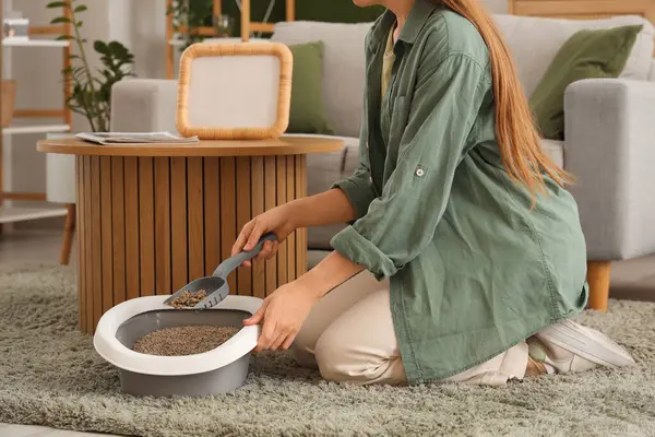 Kadın kedi sahibi evde çöp kutusunu değiştiriyor.