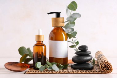 Spa taşları, bambu hasırı, okaliptüs şişeleri esaslı yağ ve kozmetik ürünler beyaz arka planda, yakın plan